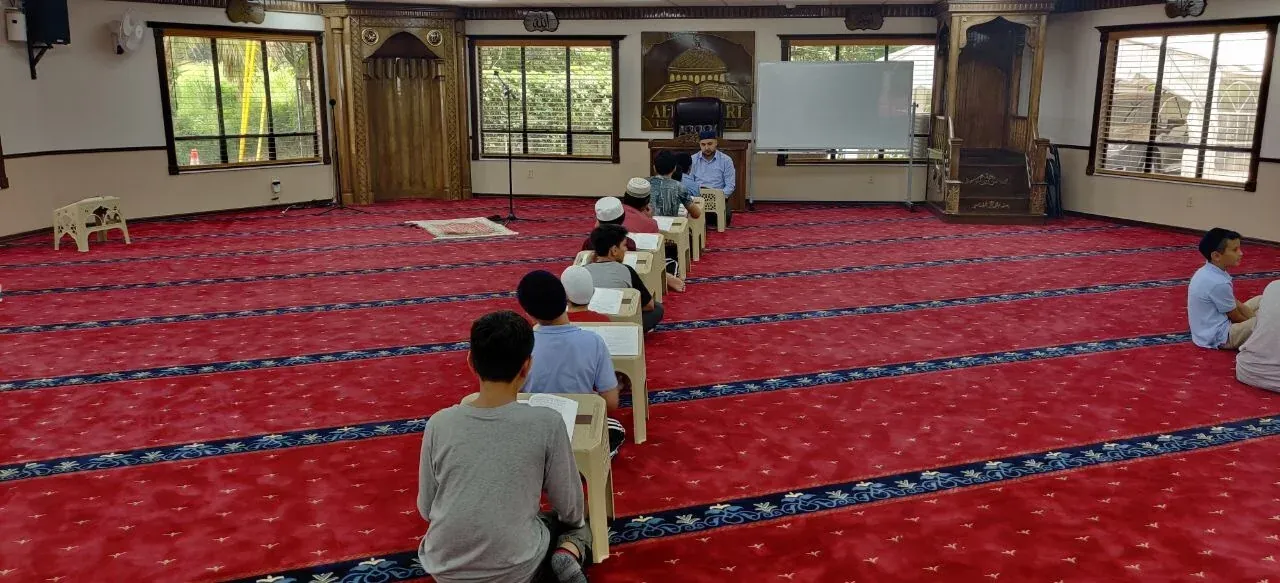 Students seated at low desks during a class in the Al Bukhari Islamic Center prayer hall